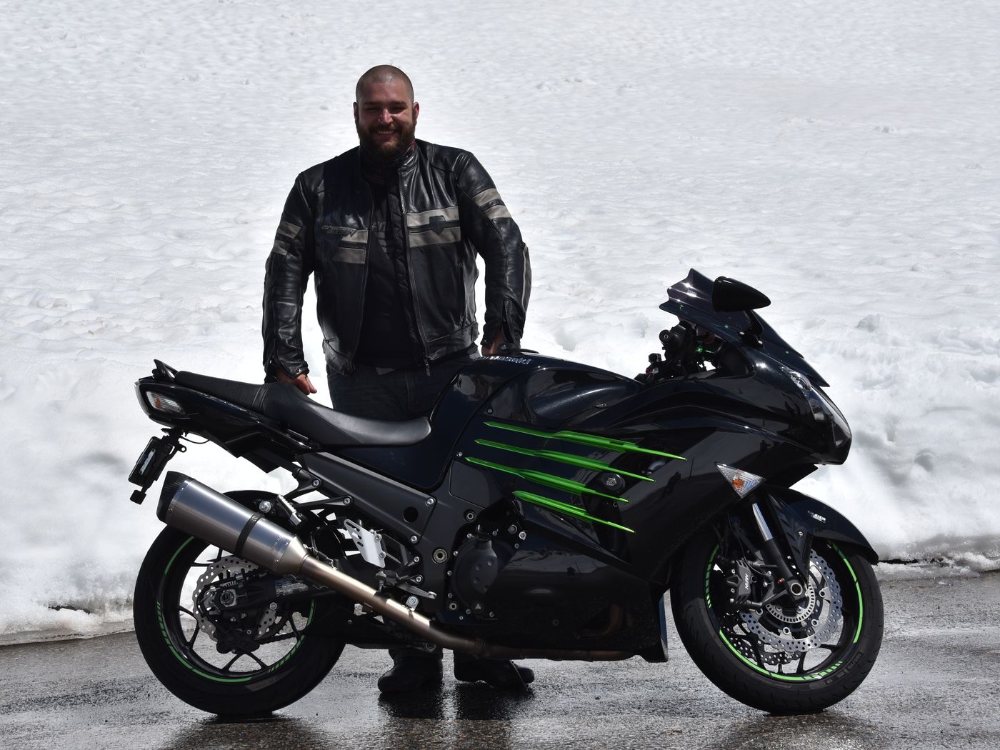 Steffen Broszeit neben seinem Motorrad auf einer Passstrasse mit Schnee